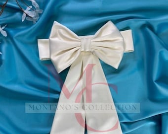May include: A white satin sash with a large bow. The sash is tied in a bow at the center and the ends are left long and flowing. The sash is on a blue background.