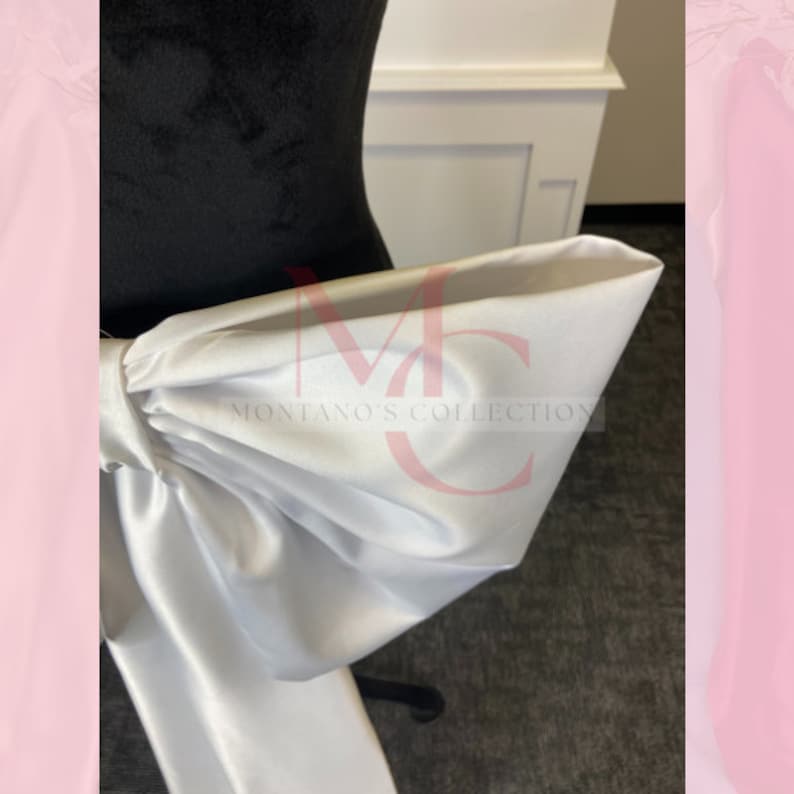 May include: A white satin bow tied around a black dress form. The bow is large and has a lot of volume. The text "MONTANO'S COLLECTION" is visible on the bow.