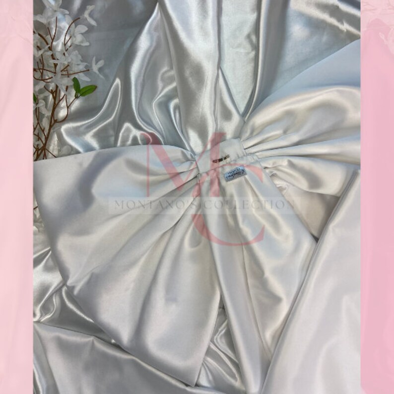 May include: A large white satin bow with a small silver tag that reads "MONTANO'S COLLECTION".