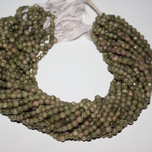以下が含まれることがあります： 緑色の蛇紋石ビーズのストランド。各ビーズは丸く、わずかにざらざらした質感です。