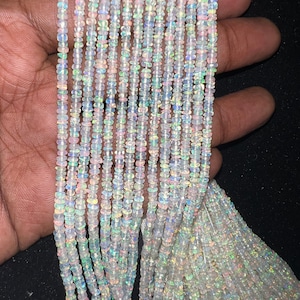May include: A strand of white opal beads with iridescent rainbow flashes. The beads are small and round, and the strand is long enough to make a necklace or bracelet.