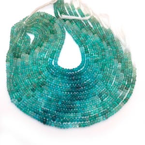May include: Strands of small, round beads in shades of teal and green. The beads are strung together, creating a layered effect. The beads are on a white background.