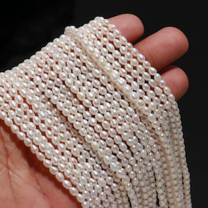 May include: Strands of small, white, oval-shaped pearls. The pearls are strung together, creating a cascading effect. The pearls have a lustrous sheen, reflecting light. The background is dark, which makes the pearls stand out.