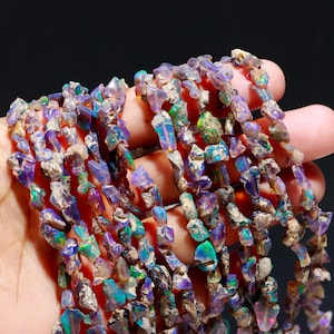 May include: A strand of iridescent opal gemstone beads. The beads are irregular in shape and have a mix of purple, blue, green, and gold tones.