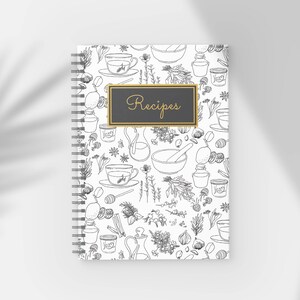 Pu&ograve; includere: Un quaderno di ricette a spirale con una copertina bianca con un motivo a linee in bianco e nero di erbe, tazze da t&egrave; e utensili da cucina. Il quaderno ha un rettangolo nero con finiture dorate e la parola "Recipes" in corsivo dorato.