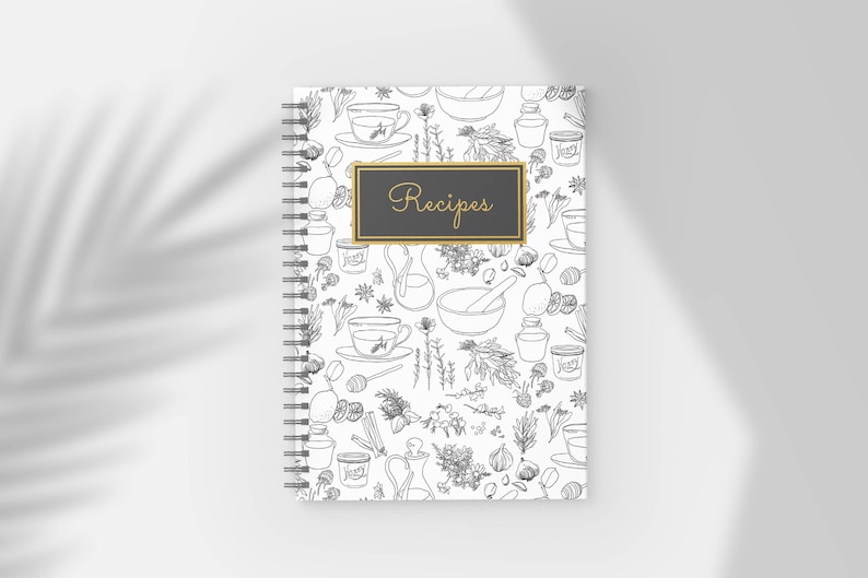 Pu&ograve; includere: Un quaderno di ricette a spirale con una copertina bianca con un motivo a linee in bianco e nero di erbe, tazze da t&egrave; e utensili da cucina. Il quaderno ha un rettangolo nero con finiture dorate e la parola "Recipes" in corsivo dorato.