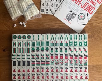Puede incluir: Un juego de Mahjong completo con fichas, dados y folletos de instrucciones. Las fichas son blancas con símbolos verdes, rojos y negros. Los folletos se titulan "Mah-Jongg" y "Directions of Playing Mah-Jong".