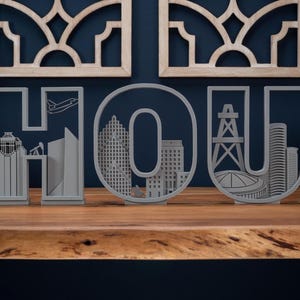 May include: Gray wooden decorative letters spelling "HOU" with city skyline cutouts. The letters sit on a wooden surface with a dark blue background. Decorative wooden wall art is in the background.