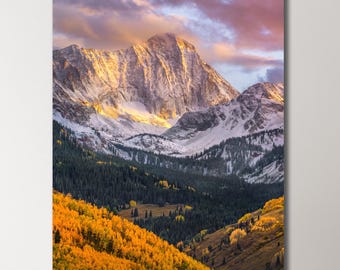 May include: A mountain peak with snow-capped peaks and a golden sunset over a valley with yellow and green trees.