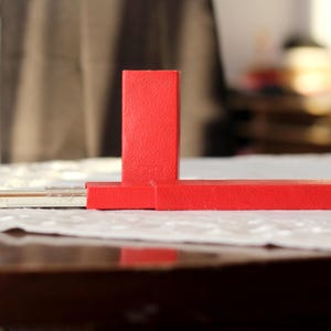 May include: A red rectangular box with a smaller red box on top. The box is sitting on a white tablecloth.