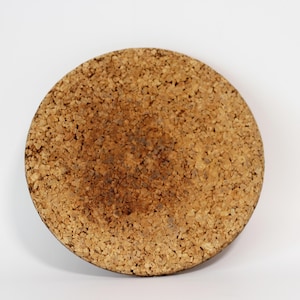 Può includere: Un sottobicchiere rotondo in sughero con una superficie strutturata. Il sottobicchiere è di colore marrone chiaro con aree marroni più scure al centro. È progettato per proteggere le superfici da calore e umidità.