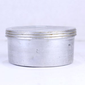 Peut inclure: Un récipient en aluminium argenté avec un couvercle à trois crêtes. Le récipient est rond et a une surface lisse.