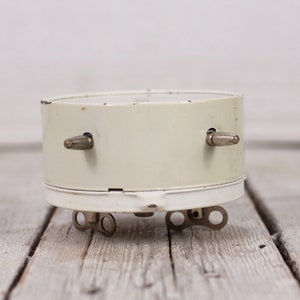 May include: A white vintage alarm clock with silver knobs on the side. The clock is sitting on a light wood surface.