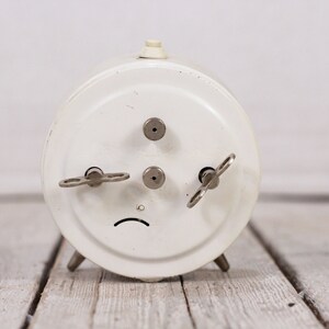 May include: White vintage wind-up alarm clock with three keys on the back.