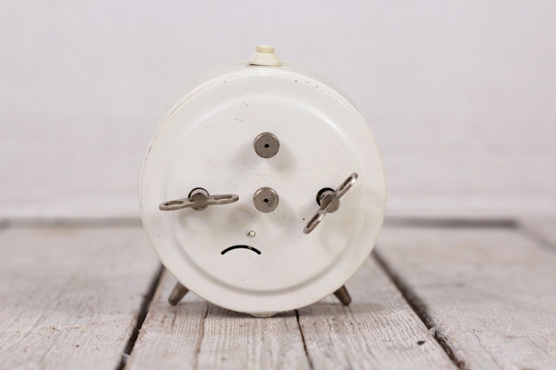 May include: White vintage wind-up alarm clock with three keys on the back.