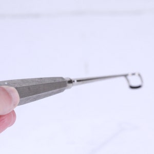 Puede incluir: Un instrumento médico de plata con un mango largo y delgado y un bucle en el extremo.