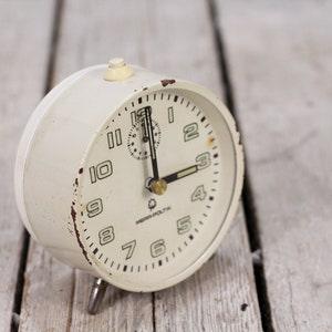 May include: White vintage alarm clock with black hands and numbers. The clock face has the text "MEWA POLTK" printed on it.