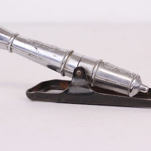 May include: A silver-colored metal toy cannon with a black metal base. The cannon has a detailed design and is in a firing position.