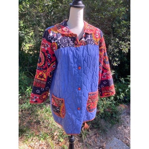 May include: A blue quilted jacket with a patchwork design. The jacket has a button closure and two patch pockets. The patchwork design features red, orange, yellow, black, and white floral patterns.