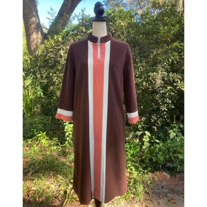 May include: A brown vintage dress with a mandarin collar and long sleeves. The dress features a vertical stripe design in white and coral down the front, with matching accents on the sleeves. The dress is displayed on a mannequin.