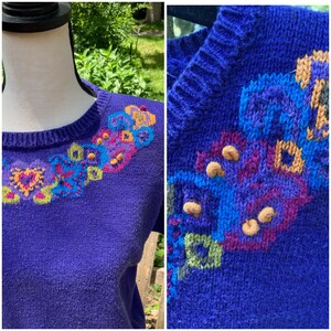Puede incluir: Un su&eacute;ter de punto morado con un dise&ntilde;o floral colorido alrededor del cuello. El dise&ntilde;o presenta una variedad de colores, incluyendo azul, verde, amarillo, naranja y rosa.