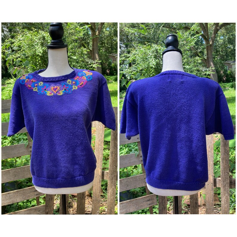 Puede incluir: Un su&eacute;ter morado de manga corta con un dise&ntilde;o floral bordado de colores alrededor del cuello.