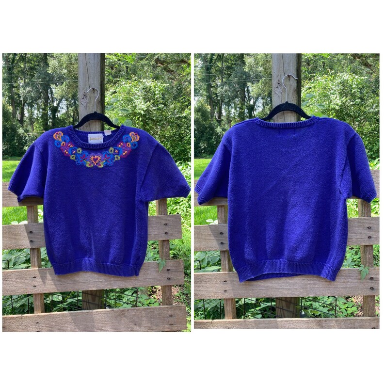 Puede incluir: Un su&eacute;ter morado de manga corta con un cuello bordado con flores de colores.