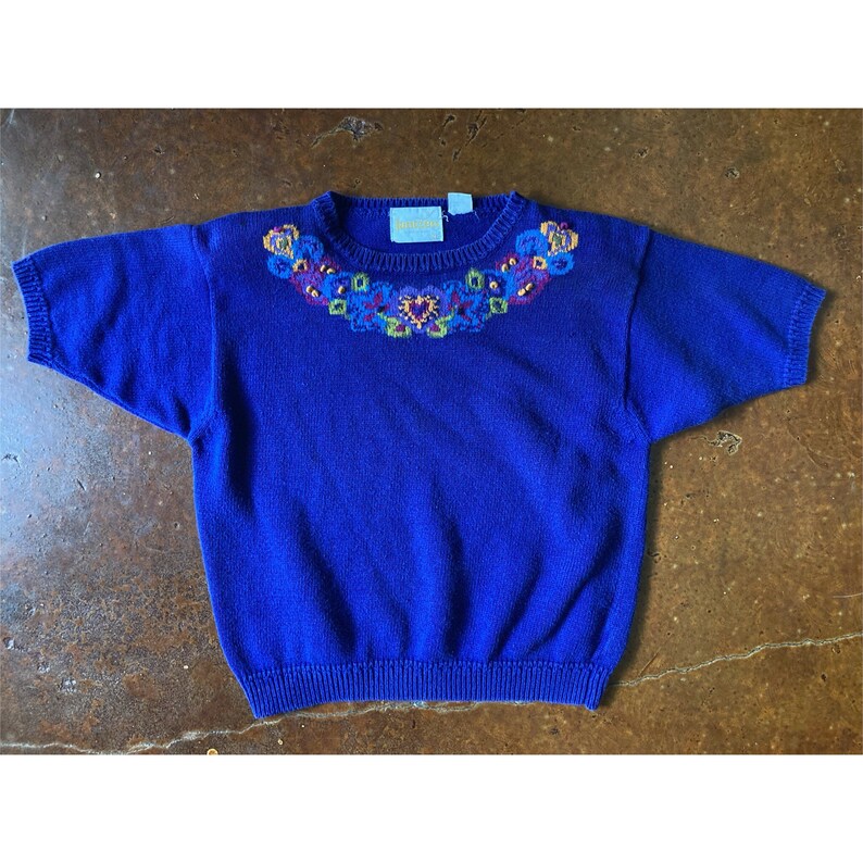 Puede incluir: Un su&eacute;ter azul real de manga corta con un cuello bordado con flores. El bordado es en tonos de amarillo, verde, rojo y azul.