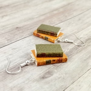 Könnte beinhalten: Ein Paar Ohrringe in Buchform mit silbernen Haken. Die Bücher sind übereinander gestapelt und haben einen grünen und orangefarbenen Einband.