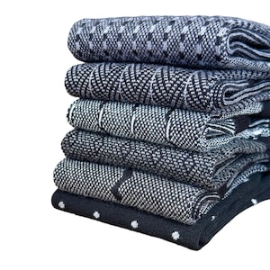 May include: A stack of six folded socks in shades of black, gray, and white. Each pair features a distinct knit pattern, including geometric shapes, chevron lines, vertical stripes, textured weaves, and a final pair with small white polka dots.