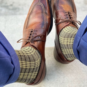 May include: A pair of brown leather dress shoes with a yellow and brown plaid pattern on the socks.