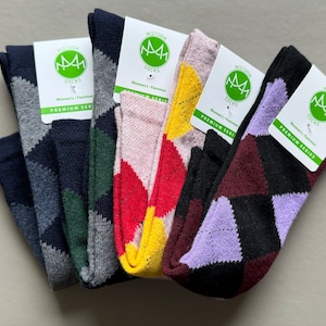 Op de afbeelding: Vijf paar sokken met argyle-patronen in verschillende kleuren. De sokken zijn gevouwen en in een rij gerangschikt. Elk paar heeft een label met de woorden "Mistorm Socks" en "Premium Series".