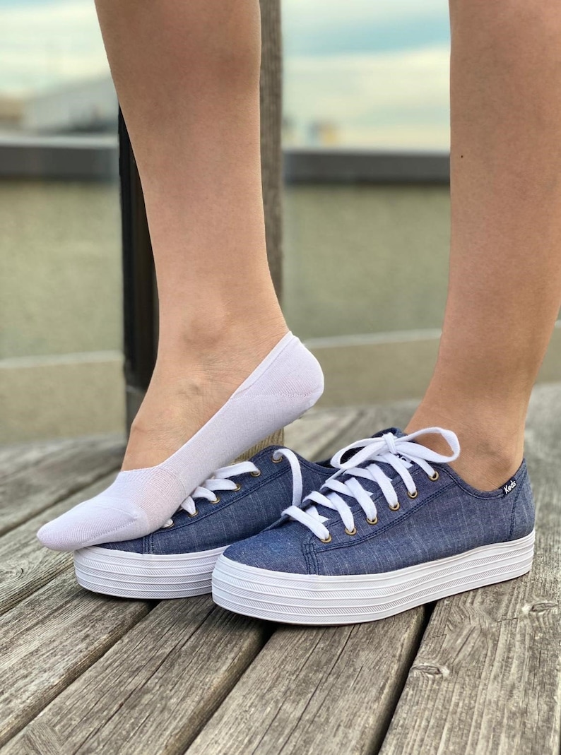 May include: A pair of white no-show socks with a pair of blue denim platform sneakers with white laces and a white sole. The sneakers have the word "Keds" on the side.