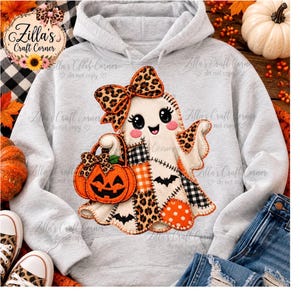 Puede incluir: Una sudadera con capucha gris claro que presenta un gráfico central de un fantasma de dibujos animados con un lazo de estampado de leopardo. El fantasma sostiene una calabaza naranja y tiene parches de estampado de leopardo, cuadros y lunares.