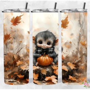 May include: A stainless steel tumbler with a fall-themed design featuring a cute monkey holding a pumpkin. The background is a watercolor-style illustration of leaves and branches in shades of brown, orange, and yellow.