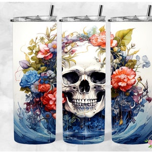 May include: A white stainless steel tumbler with a colorful floral design and a skull in the center. The flowers are red, blue, and yellow. The skull is white with black eyes and a black mouth. The tumbler is sitting on a white background.
