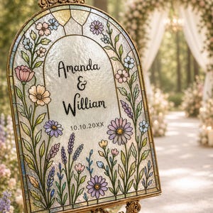 Può includere: Un cartello nuziale in vetro colorato con i nomi "Amanda & William" e la data "10.10.20XX". Il cartello presenta un design floreale con fiori rosa, viola e blu, incorniciato in oro. Il cartello è esposto su un cavalletto decorativo.