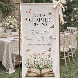 Puede incluir: Una pancarta de lino crema con el texto "A New Chapter Begins" y "Welcome to Olivia's Baby Shower". La pancarta está decorada con mariposas y un libro abierto con ilustraciones florales. El evento es en Viena, Austria.