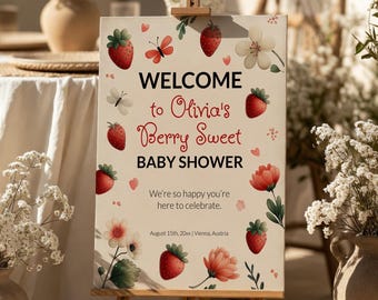 May include: A wooden easel displays a baby shower sign. The sign reads "WELCOME to Olivia's Berry Sweet BABY SHOWER" with strawberry and floral illustrations. The sign also includes the text "We're so happy you're here to celebrate."
