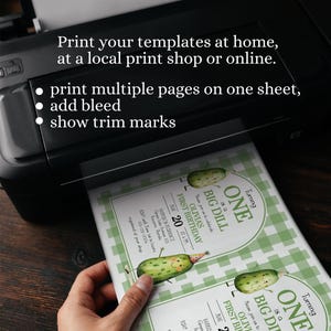 Op de afbeelding: Een zwarte printer die uitnodigingen afdrukt. De uitnodigingen hebben een groen-wit ruitpatroon en een cartoon augurk ontwerp met de tekst "Turning ONE is a BIG DILL". De tekst op de uitnodiging luidt "OLIVIA'S FIRST BIRTHDAY".