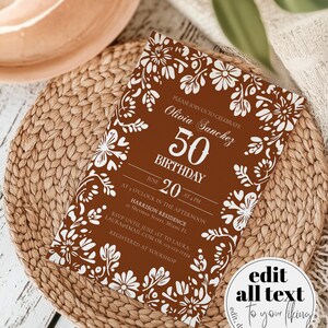 Peut inclure: Une invitation d'anniversaire marron avec des motifs floraux blancs et du texte. L'invitation indique "Olivia Sanchez 50e anniversaire le 20 juin &agrave; 16h". L'invitation est sur un tapis tress&eacute;.