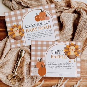 May include: Two baby shower invitation cards with a fall theme. One card reads "Books for our Baby Noah" and the other says "Diaper Raffle". Both cards feature illustrations of pumpkins and a turkey. A gold wax stamp and coins are also visible.