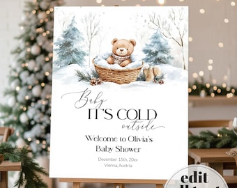 Może przedstawiać: Prostokątny znak z akwarelową ilustracją brązowego pluszowego misia w wiklinowym koszu otoczonym śniegiem i sosnami. Tekst brzmi: Baby IT'S COLD outside, Welcome to Olivia's Baby Shower, 15 grudnia 20xx, Wiedeń, Austria.