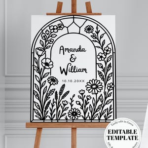 Pode incluir: Uma placa de casamento branca em um cavalete de madeira, com um design de arco floral preto. A placa exibe os nomes "Amanda & William" e a data "10.10.20XX". O canto inferior direito inclui o texto "EDITABLE TEMPLATE".