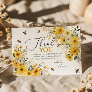 Op de afbeelding: Een bedankkaart met een bloemenontwerp met gele bloemen en bijen. De kaart heeft de woorden "Thank You" in elegant schrift, samen met een persoonlijke boodschap en handtekening. De kaart staat op een neutrale achtergrond.
