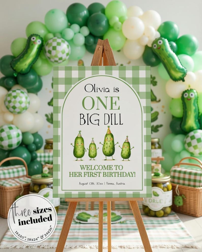 Op de afbeelding: Een houten ezel toont een bord met een groen-witte geruite rand. Op het bord staat "Olivia is ONE BIG DILL" met cartoon augurken illustraties. Groene ballonnen en augurk-vormige ballonnen versieren de achtergrond. Potten met augurken zijn ook zichtbaar.