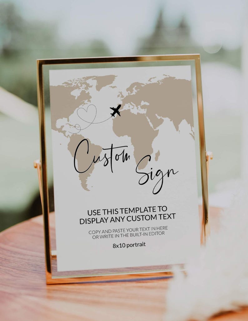 May include: A gold-framed sign featuring a world map design and the words "Custom Sign" in cursive. A heart and airplane graphic are above the text. The sign is 20.3 x 25.4 cm and includes instructions for custom text.