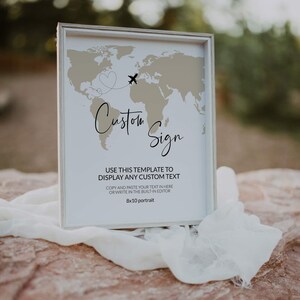 May include: A framed sign featuring a world map design, an airplane graphic, and the words "Custom Sign." The sign is 20.3 x 25.4 cm and includes instructions for adding custom text. The frame is silver.