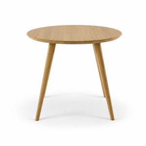 Op de afbeelding: Een ronde houten tafel met een lichtbruine natuurlijke houtnerfafwerking. De tafel heeft een glad, cirkelvormig blad dat wordt ondersteund door drie taps toelopende, schuine poten die vanuit het midden naar buiten staan voor een stabiele basis.