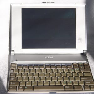 May include: A silver laptop computer with a black screen and a brown keyboard. The keyboard has keys labeled with letters, numbers, and symbols.